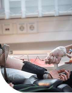 Ein Arzt führt eine Blutentnahme bei einem Patienten durch, der entspannt auf einer Liege sitzt, während seine Armvene mit medizinischen Instrumenten verbunden ist.