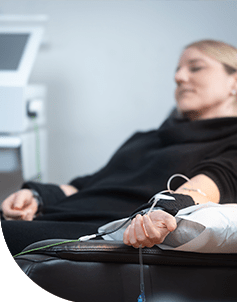 Frau erhält eine intravenöse Infusionstherapie, sitzend, entspannt mit Blick auf einen Monitor, der den Infusionsprozess überwacht.