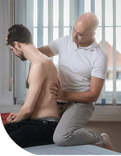 Ein osteopathischer Therapeut führt eine manuelle Rückentherapie bei einem jungen Mann durch, der auf einer Liege in einer klinischen Umgebung liegt.