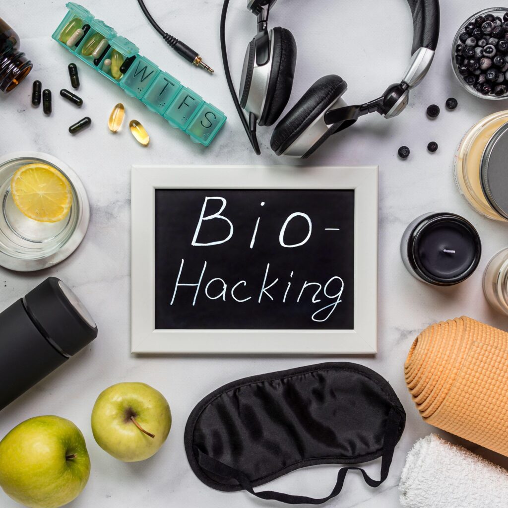 Eine kreative Darstellung des Biohacking mit einem schwarzen Bilderrahmen, der 'Bio-Hacking' beschriftet ist, umgeben von Gesundheitszubehör wie Kopfhörern, Pillendose, Zitronenwasser und Yoga-Matte.